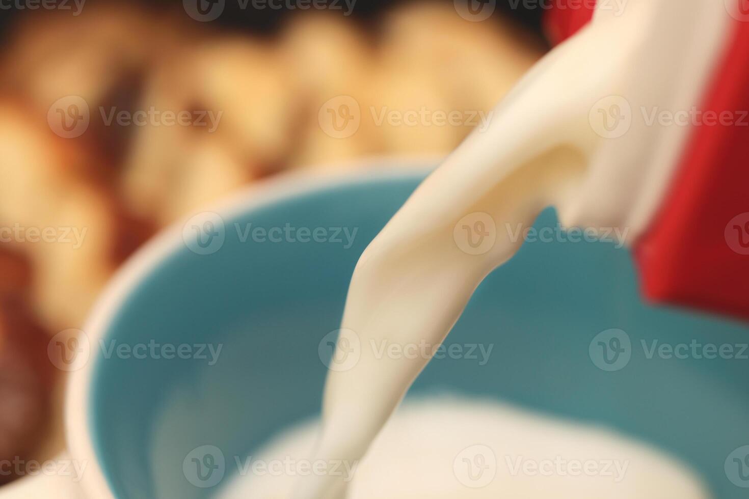 A stream of milk pours into a mug with sweet swirling roll bun slices on background. Macro closeup. photo