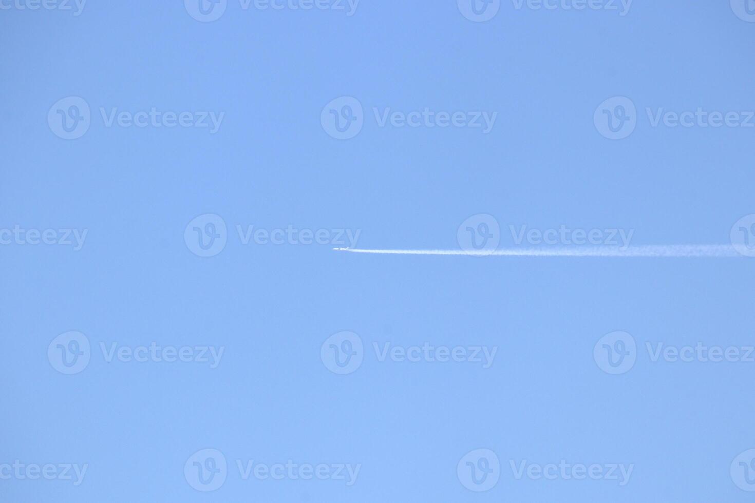 The plane flies in the clear sky, leaving a trail in a long line. photo