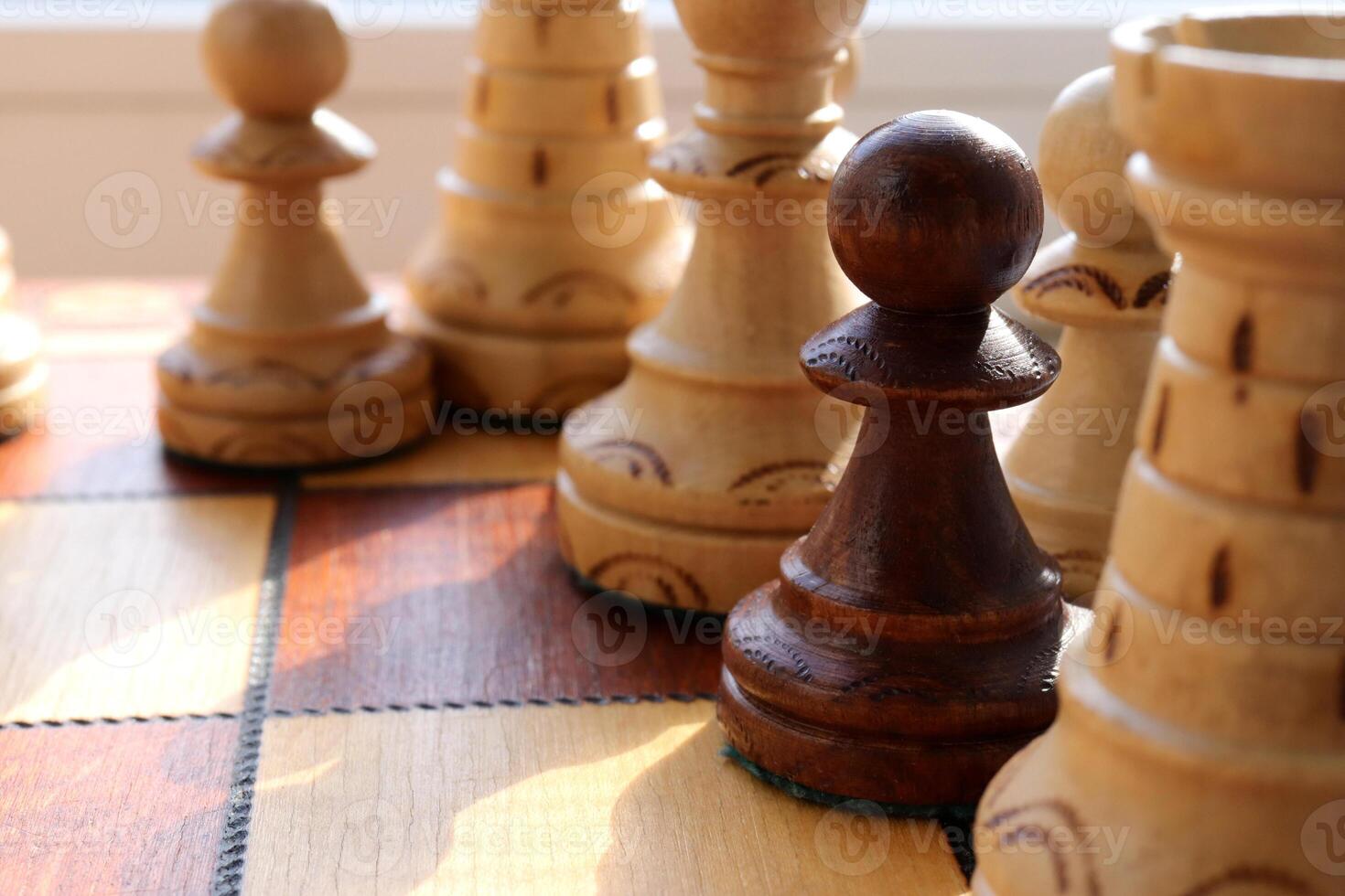 Black pawn stands among white chess figures. Wood game chessboard background. photo