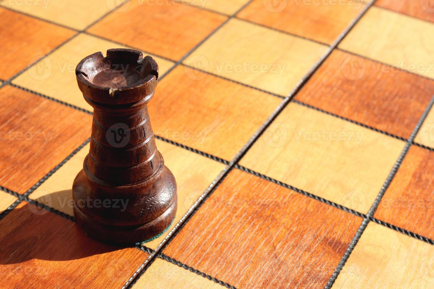 One black rook figure stands on a chess board. Wood game chessboard background. photo