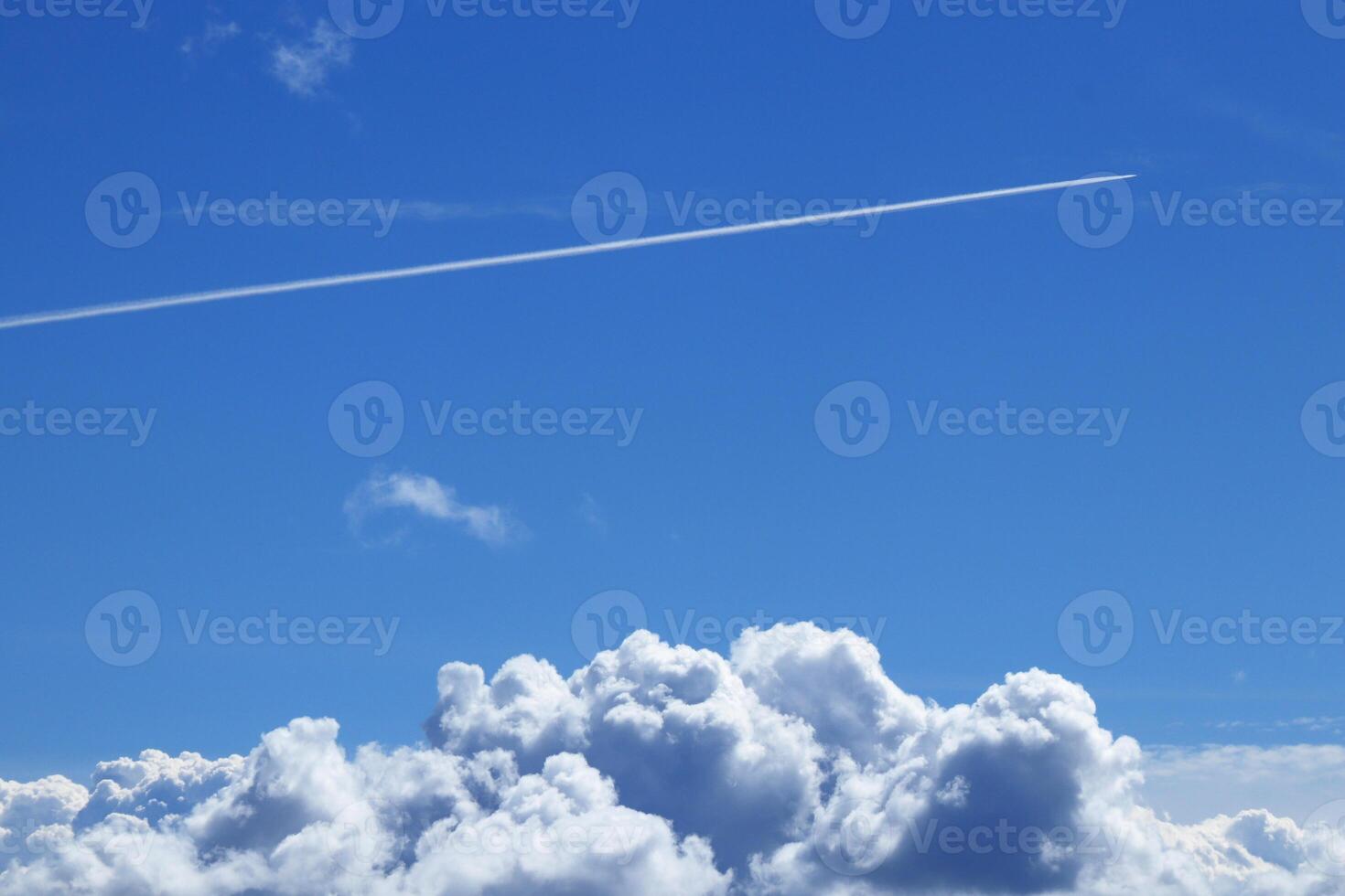 The trail of a flying airplane in a clear blue sky over large clouds. photo