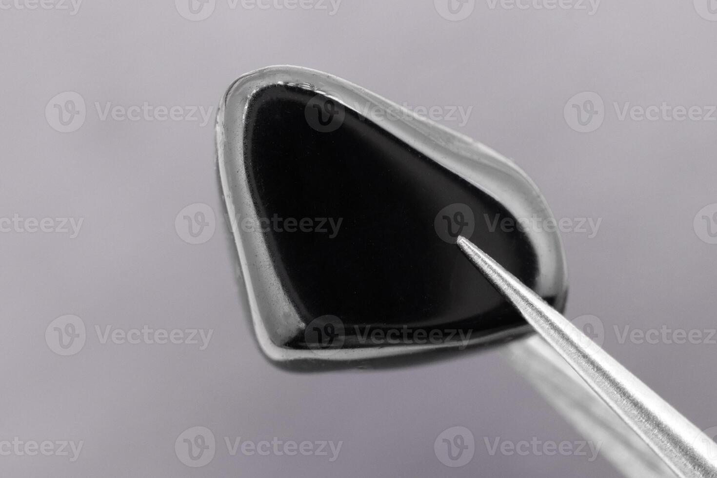 Black tourmaline jewel stone texture in tweezers on black wood background. Macro closeup. photo