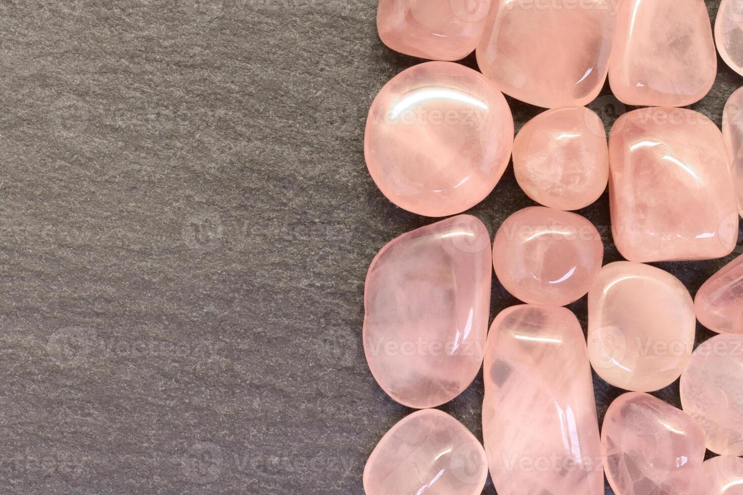 Rose quartz jewel heap on black stone half background. Pile mineral pebbles texture. Place for text. photo