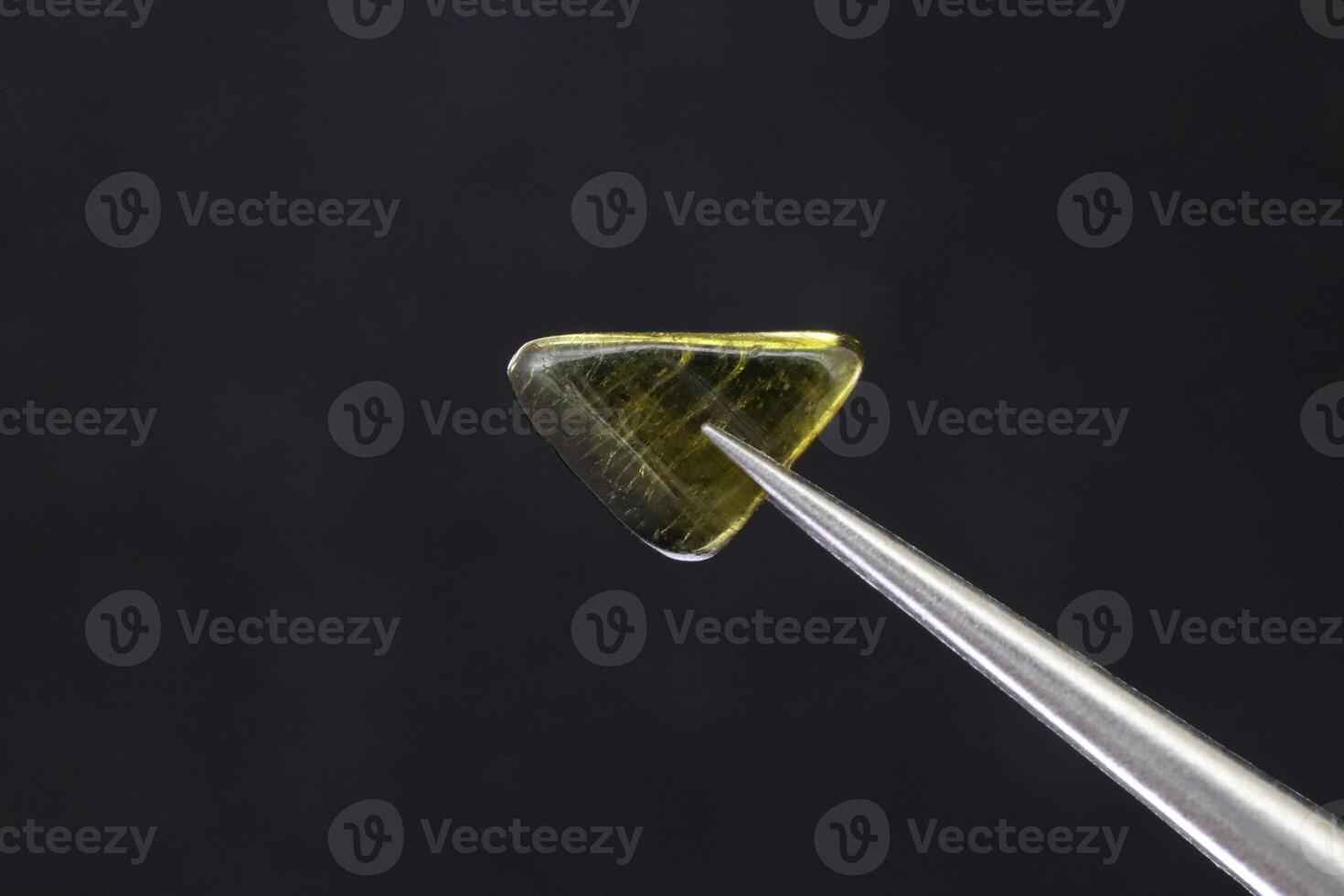Tourmaline jewel stone texture in tweezers on black background. Macro closeup. photo