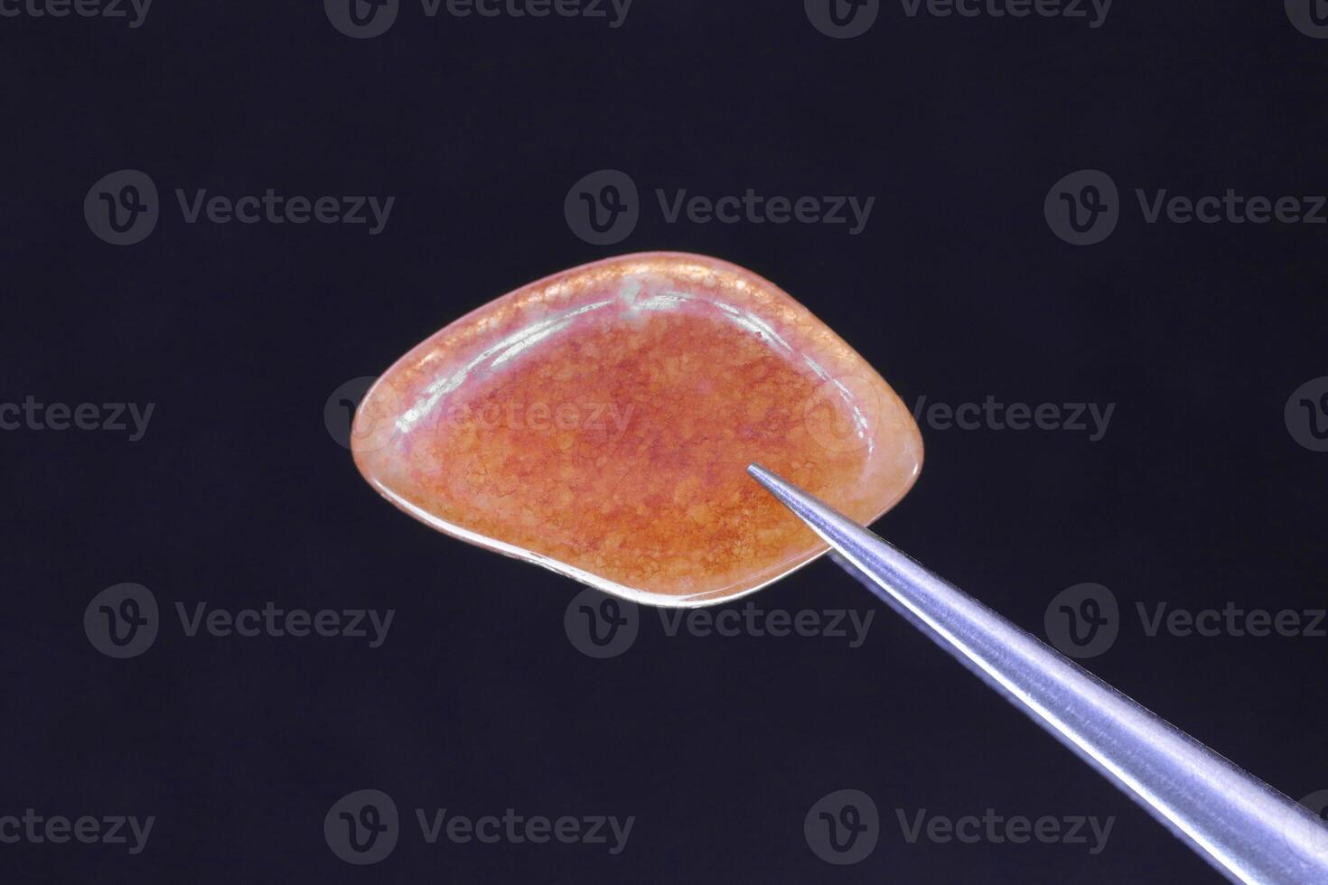 Red Aventurine jewel stone texture in tweezers on black background. Macro closeup. photo