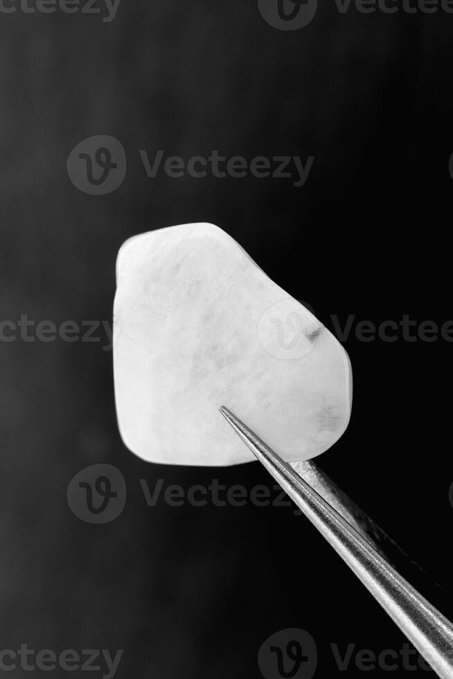 Moon stone jewel texture in tweezers on black stone background. Macro closeup. photo