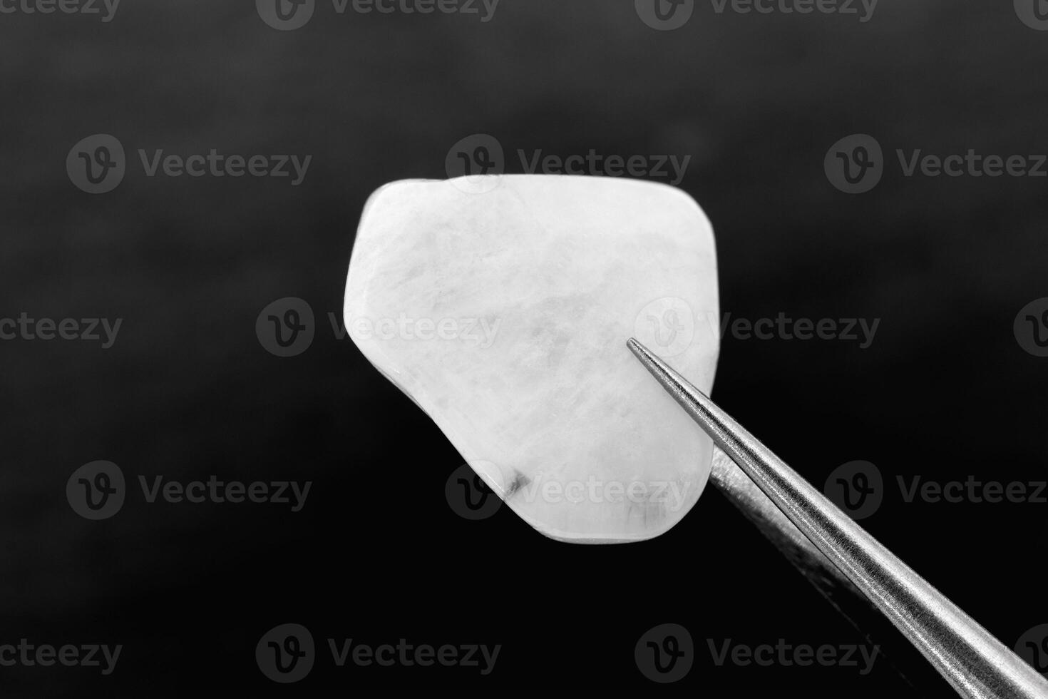 Moon stone jewel texture in tweezers on black stone background. Macro closeup. photo