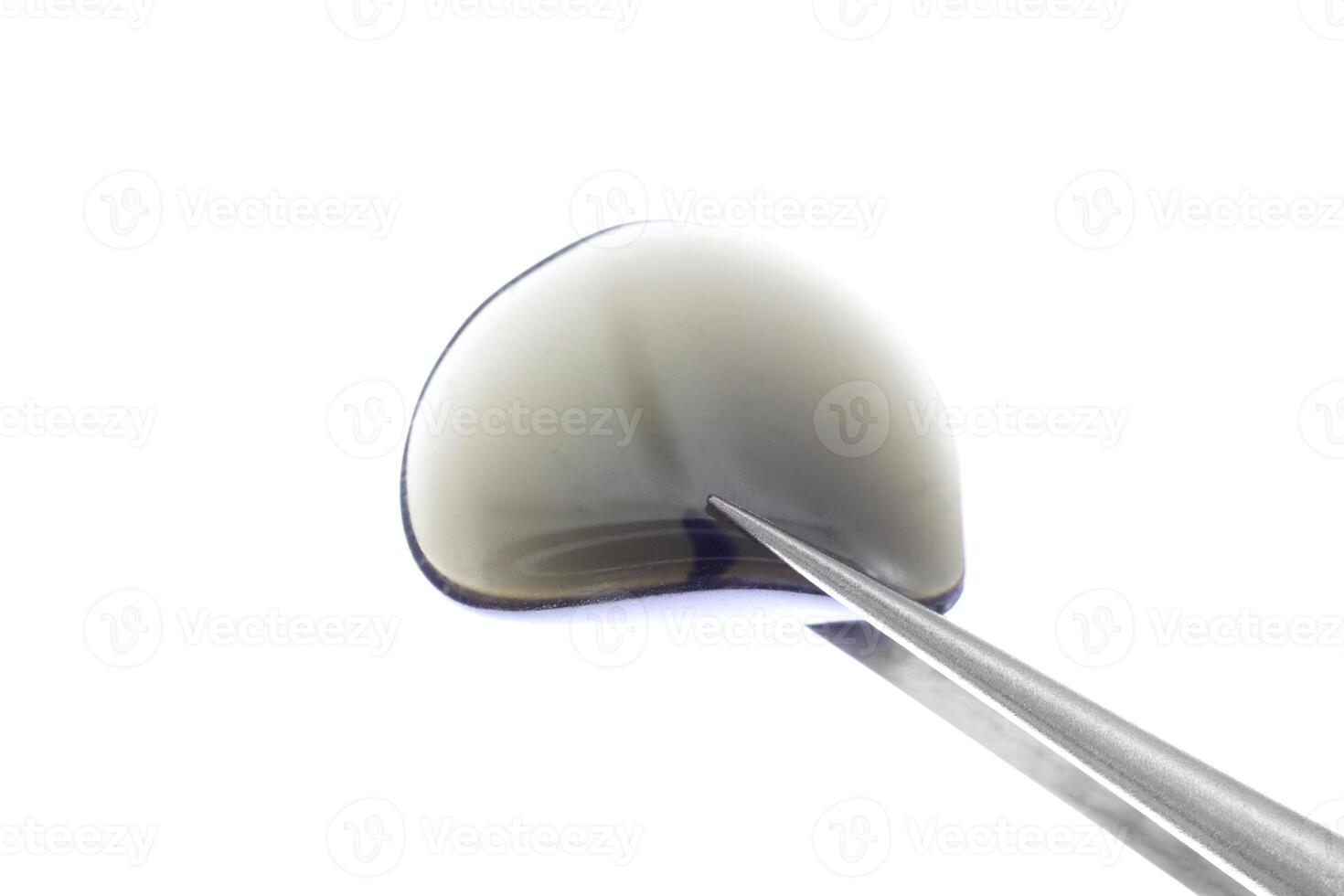 Obsidian jewel stone texture in tweezers on white light isolated background. Macro closeup. photo