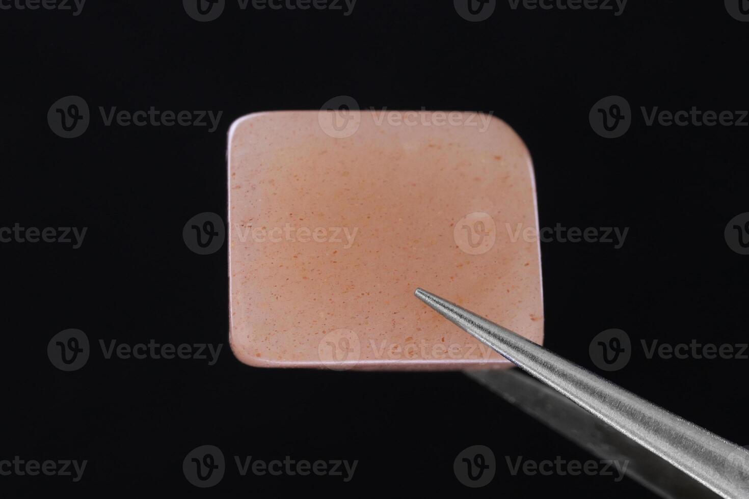 Sunstone jewel stone texture in tweezers on black background. Macro closeup. photo