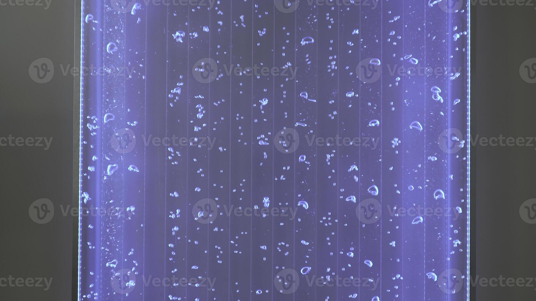 Luminous lamp with water and bubbles. Clip. Mesmerizing wall decor with glowing lamp and bubbles. Moving water bubbles in neon lamp on wall photo