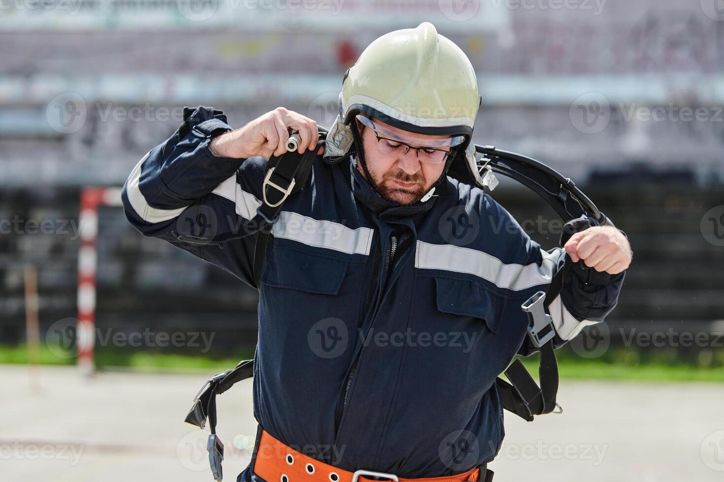 A firefighter dons the essential components of their professional gear, embodying resilience, commitment, and readiness as they gear up for a hazardous firefighting mission, a testament to their photo