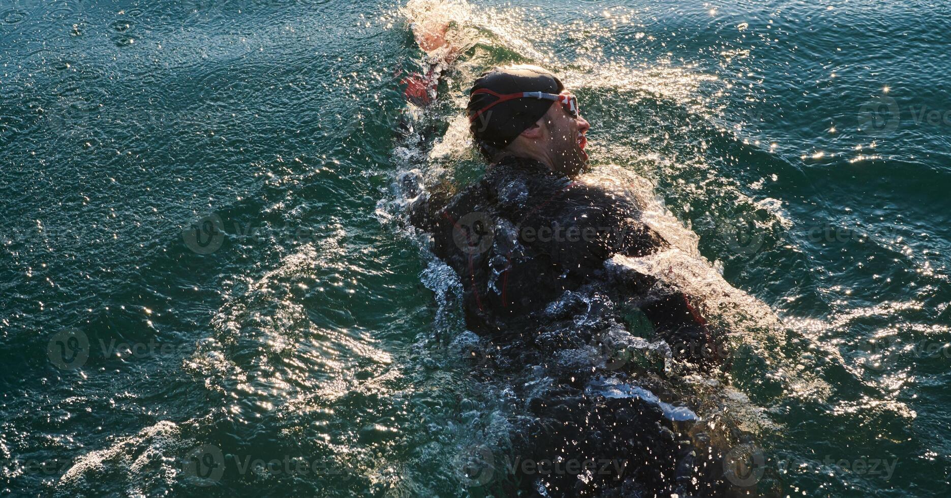 Triathlon athlete swimming on lake in sunrise wearing wetsuit photo