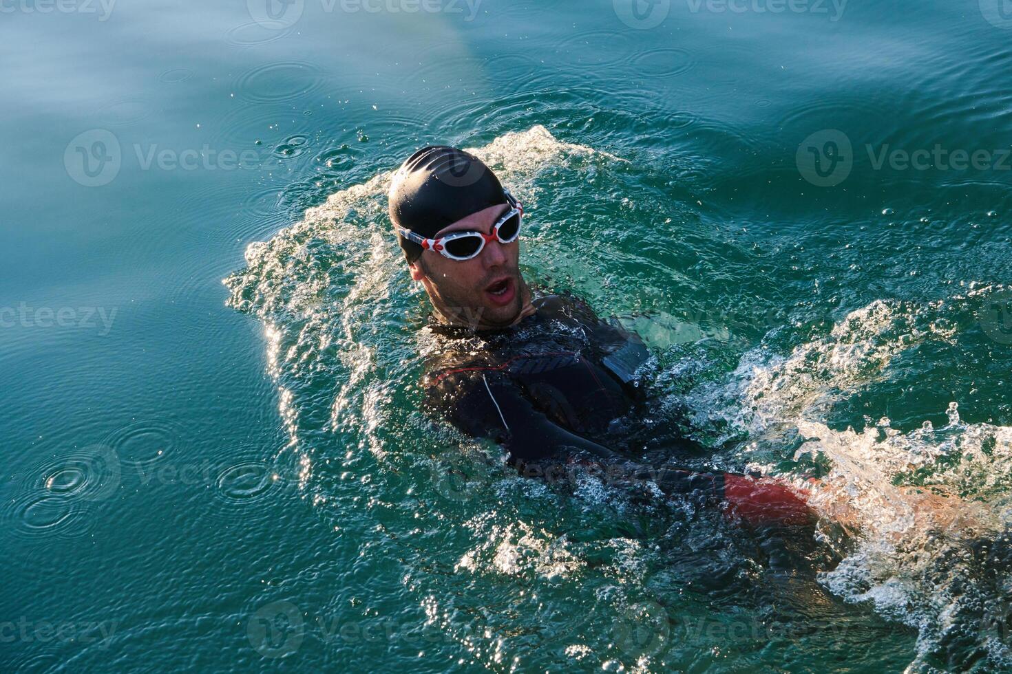 Triathlon athlete swimming on lake in sunrise wearing wetsuit photo