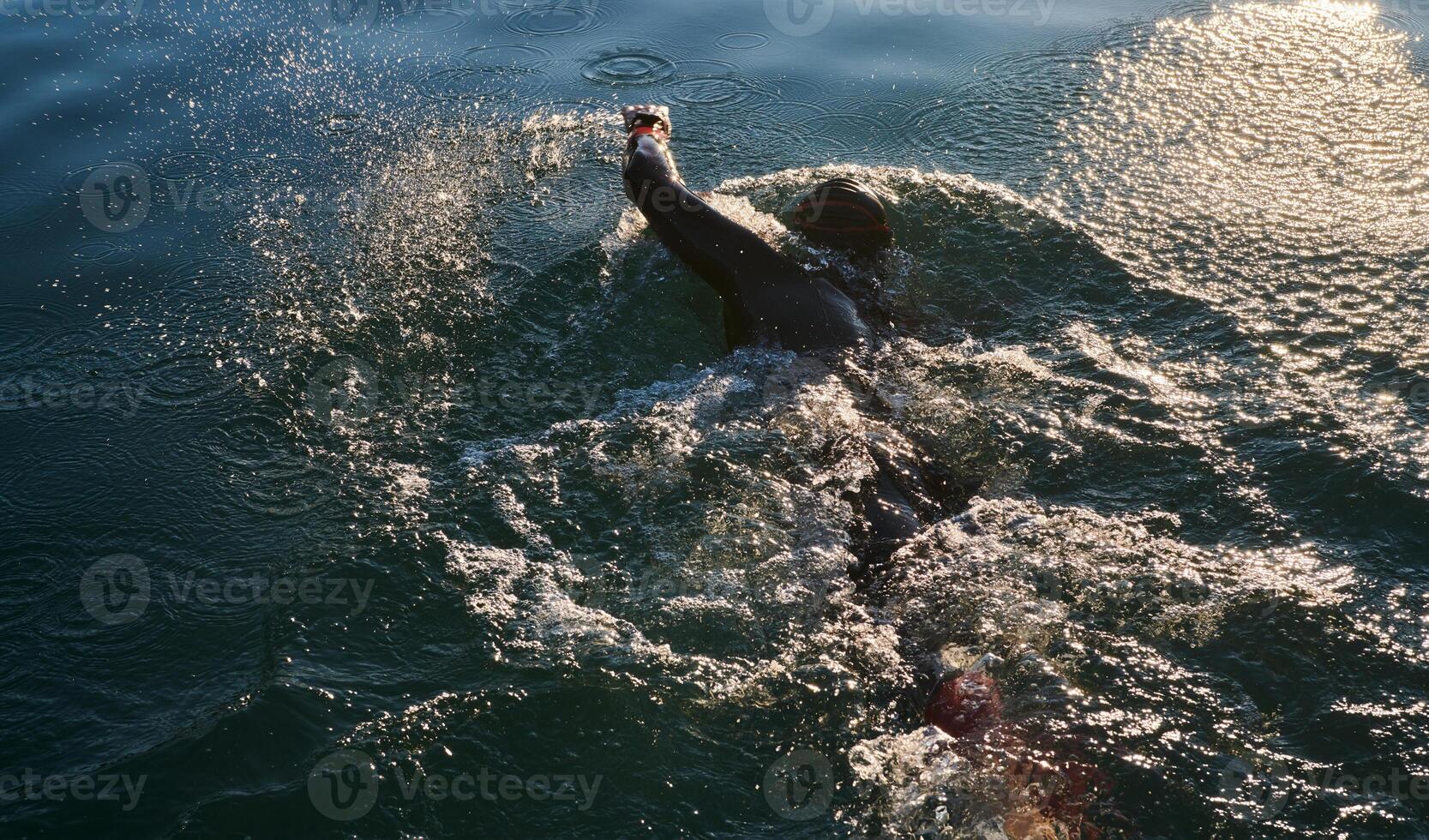Triathlon athlete swimming on lake in sunrise wearing wetsuit photo