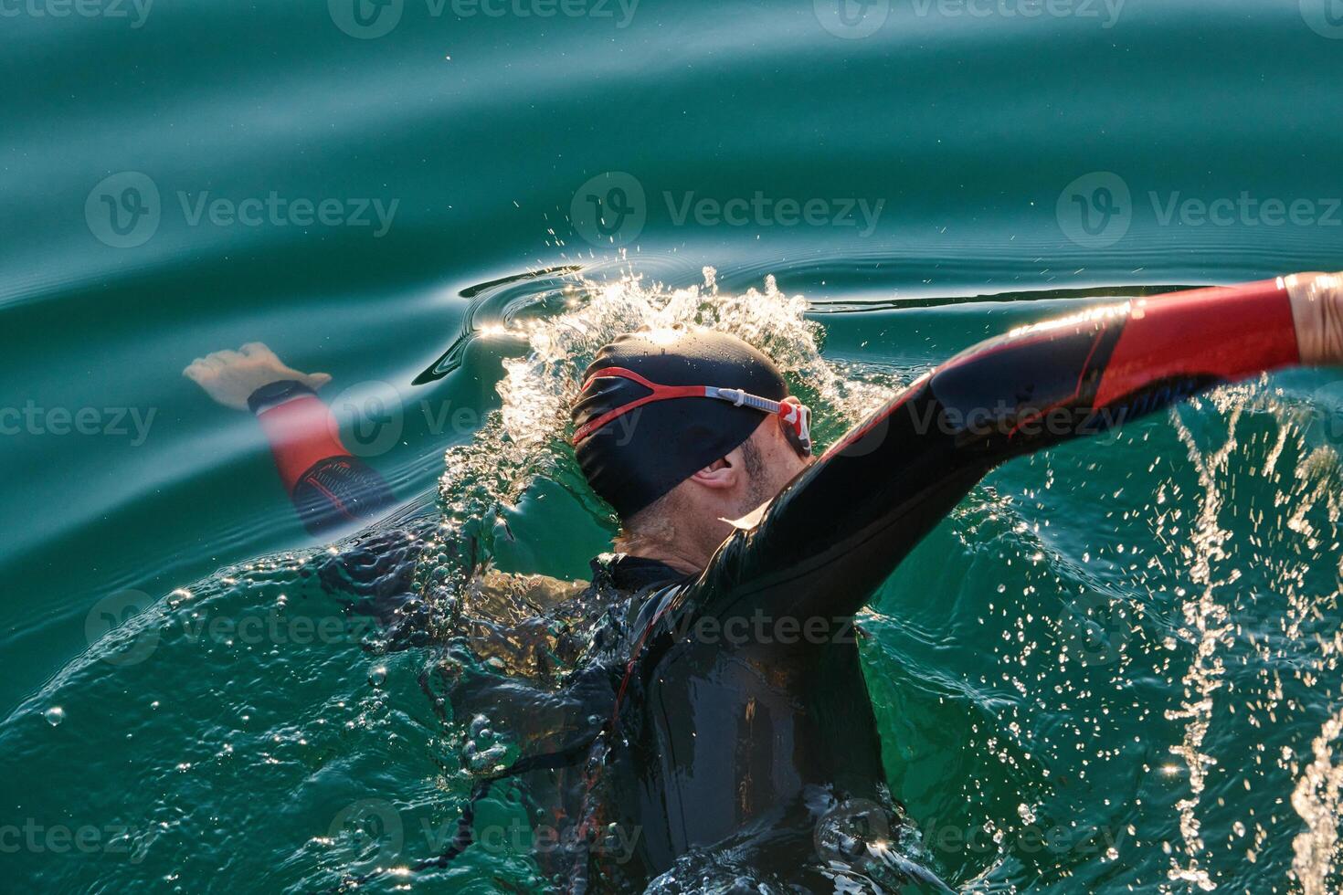 Triathlon athlete swimming on lake in sunrise wearing wetsuit photo