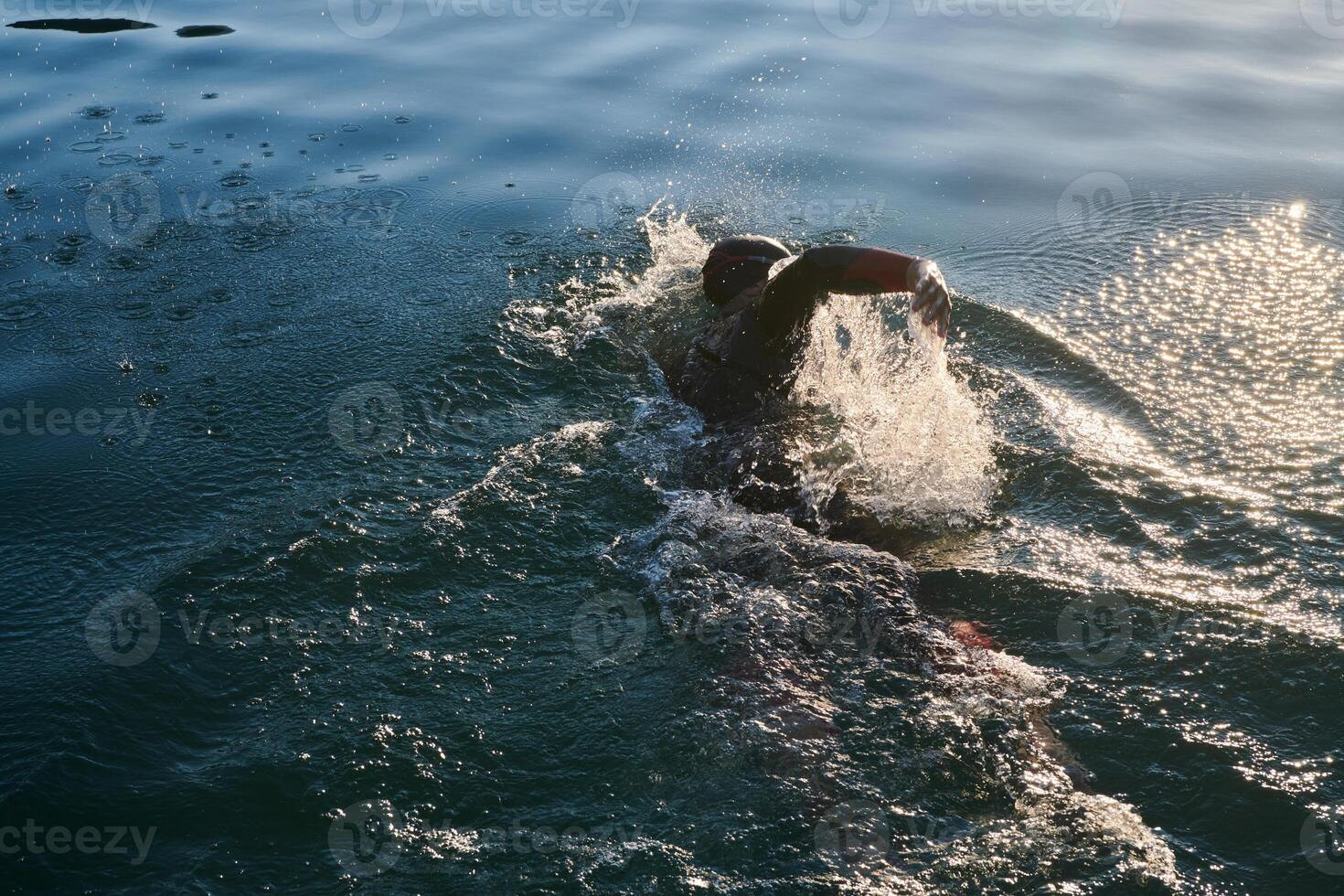Triathlon athlete swimming on lake in sunrise wearing wetsuit photo