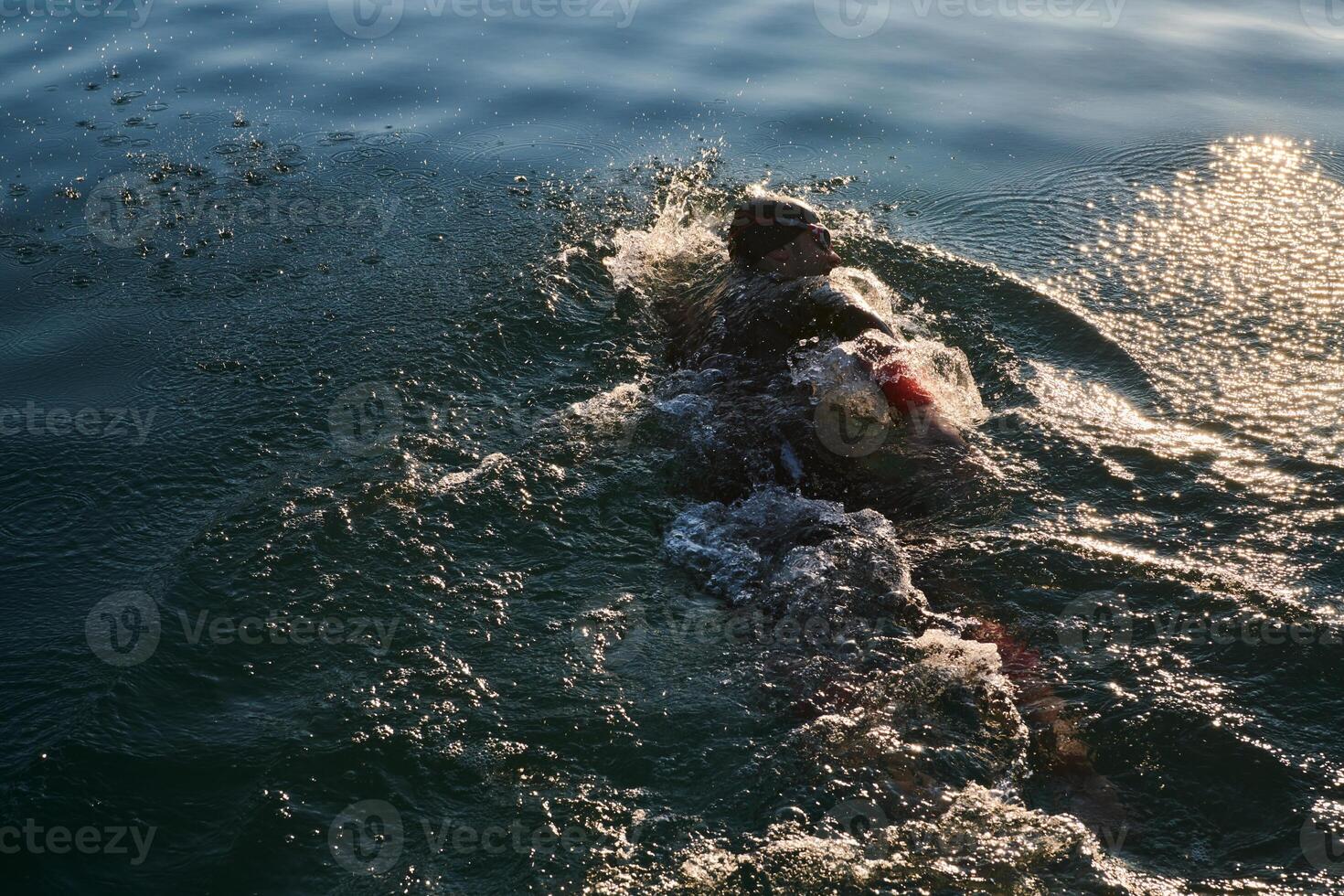 Triathlon athlete swimming on lake in sunrise wearing wetsuit photo
