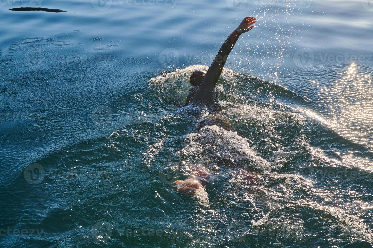 Triathlon athlete swimming on lake in sunrise wearing wetsuit photo