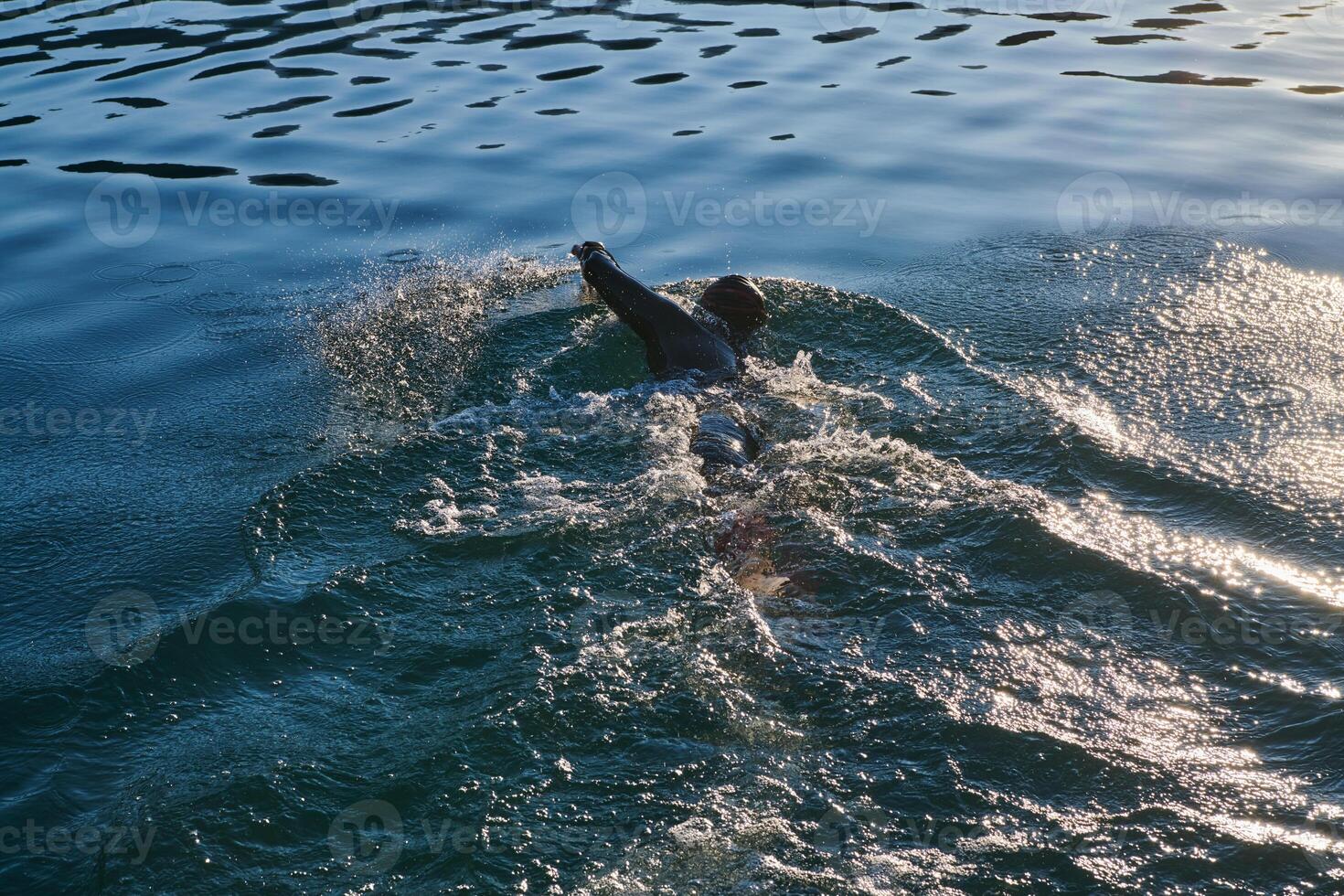 Triathlon athlete swimming on lake in sunrise wearing wetsuit photo