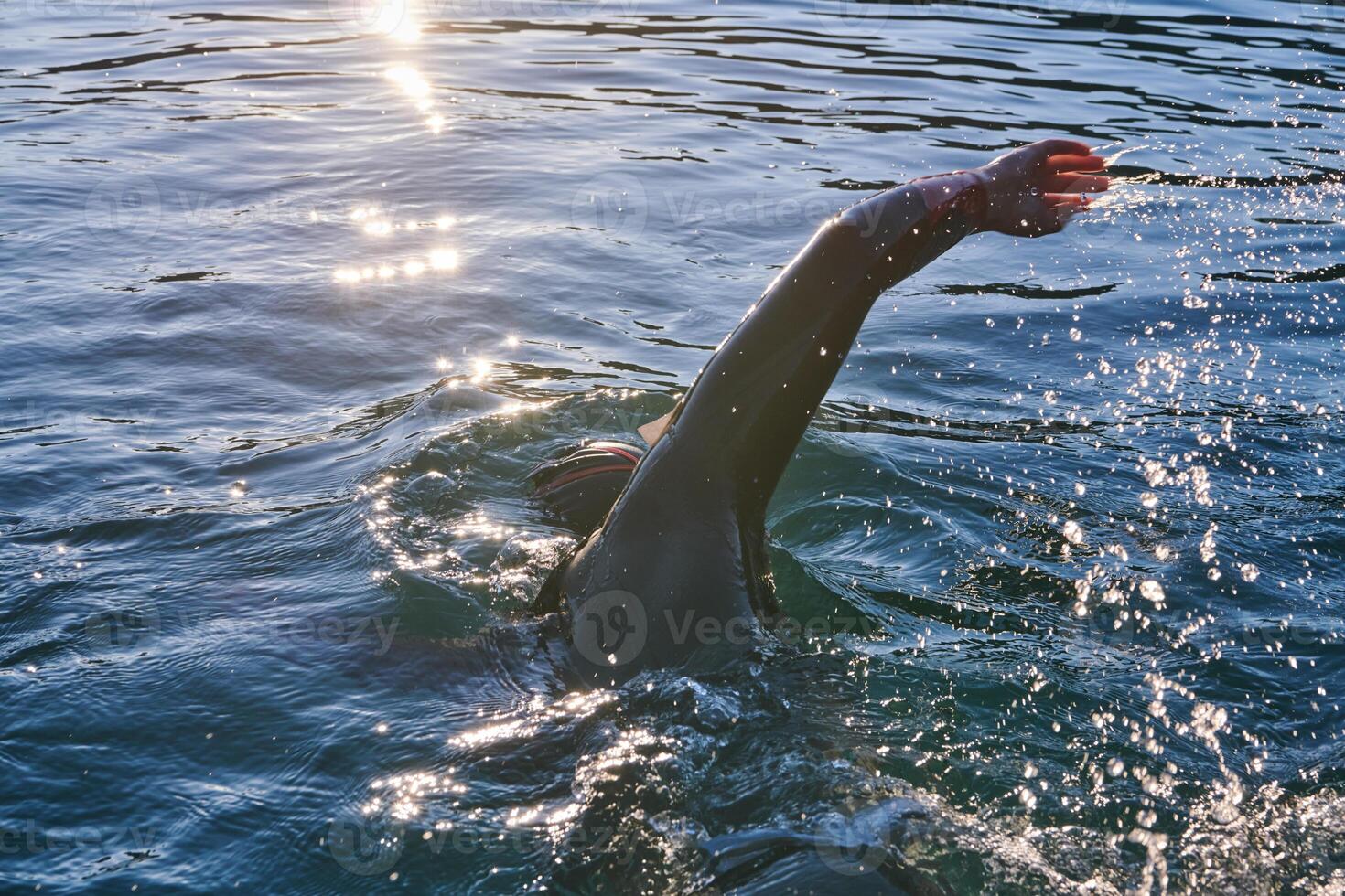 Triathlon athlete swimming on lake in sunrise wearing wetsuit photo