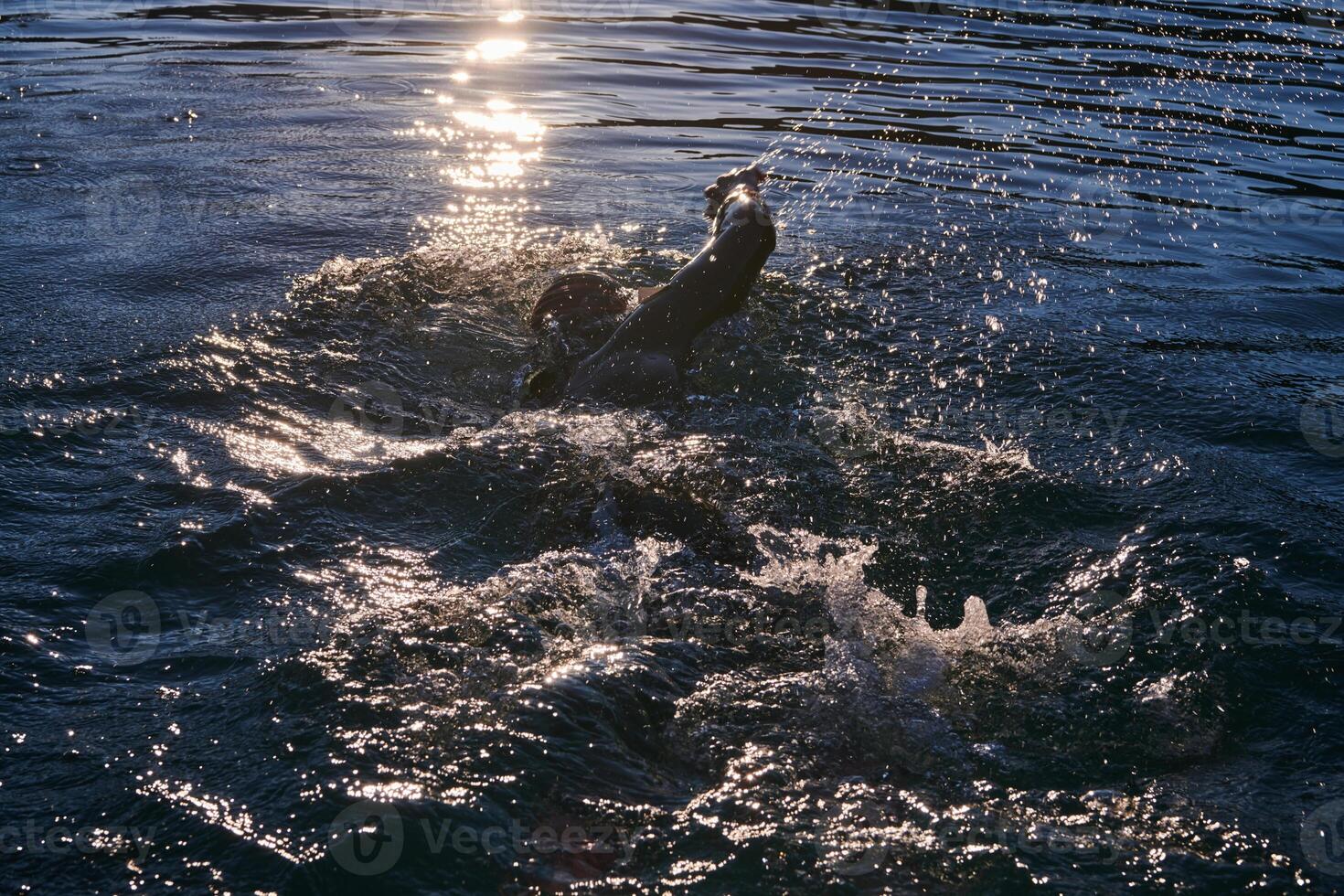 Triathlon athlete swimming on lake in sunrise wearing wetsuit photo