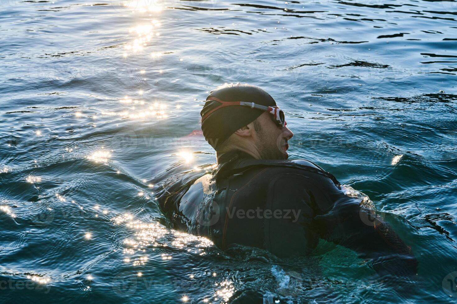 Triathlon athlete swimming on lake in sunrise wearing wetsuit photo