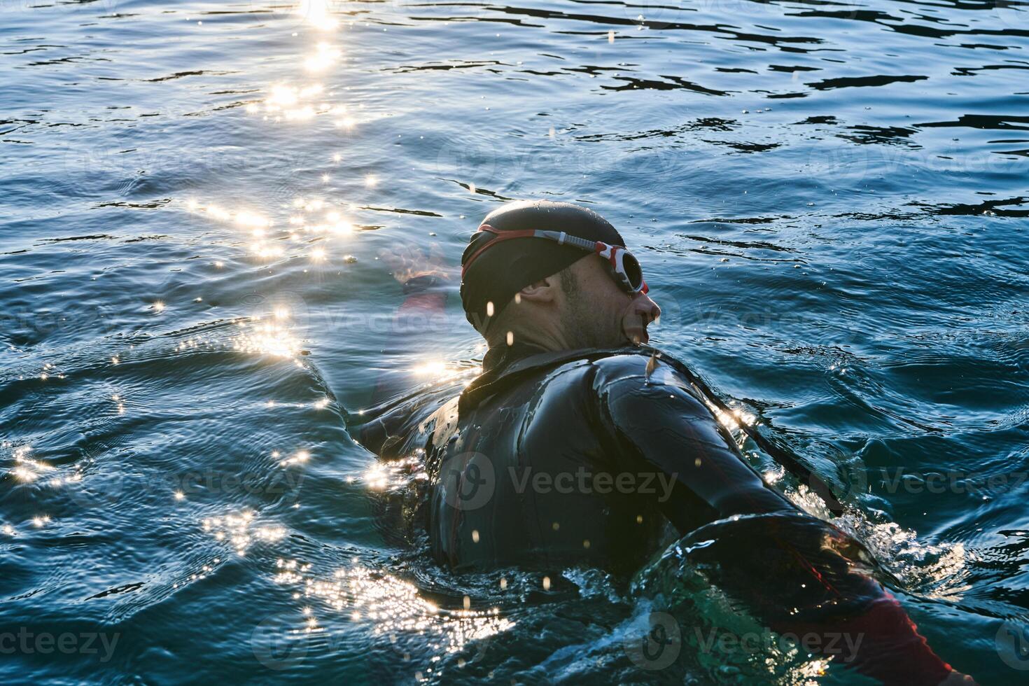 Triathlon athlete swimming on lake in sunrise wearing wetsuit photo