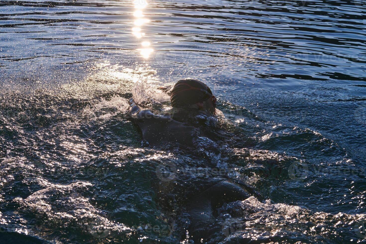 Triathlon athlete swimming on lake in sunrise wearing wetsuit photo