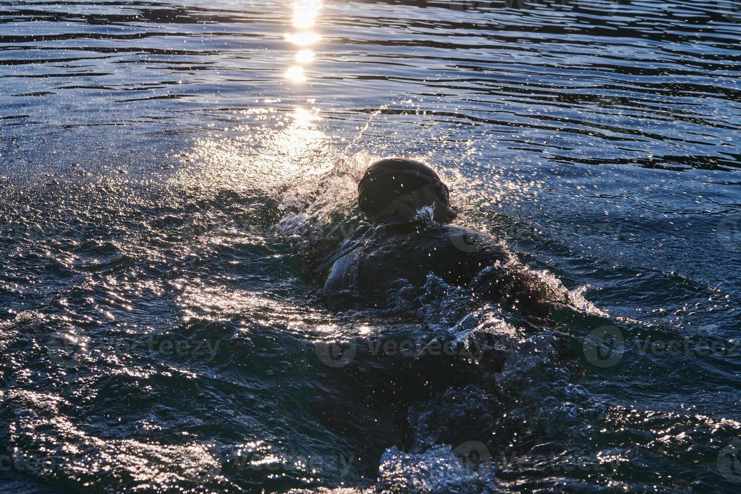 Triathlon athlete swimming on lake in sunrise wearing wetsuit photo