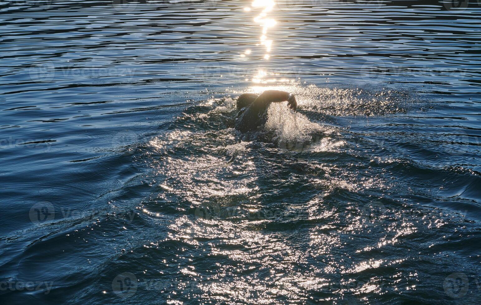Triathlon athlete swimming on lake in sunrise wearing wetsuit photo