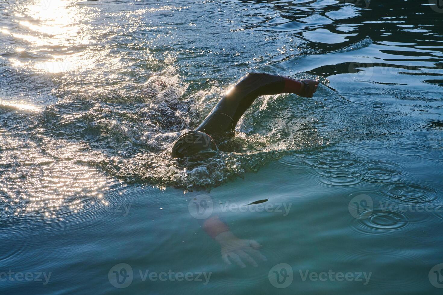 Triathlon athlete swimming on lake in sunrise wearing wetsuit photo