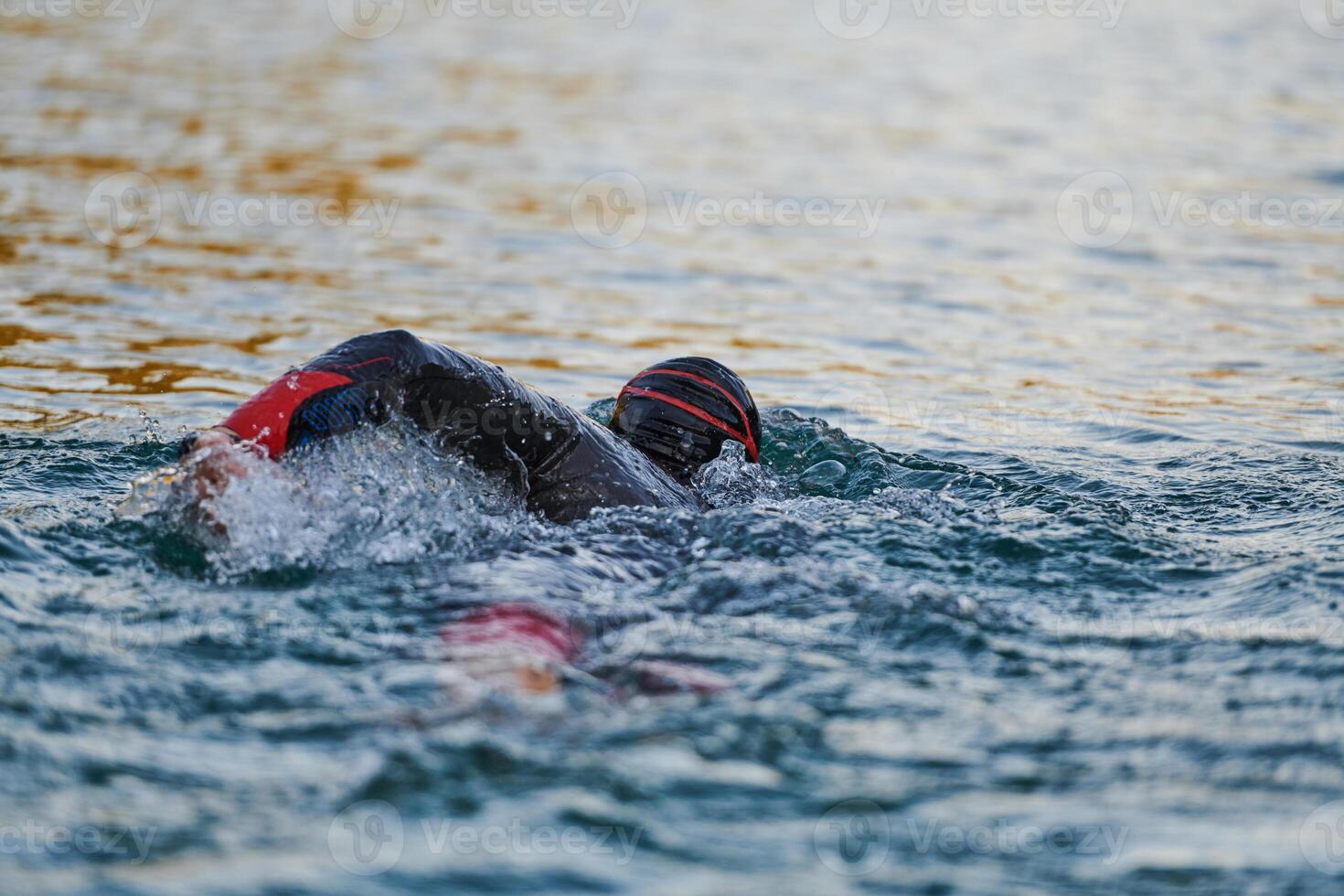 Triathlon athlete swimming on lake in sunrise wearing wetsuit photo
