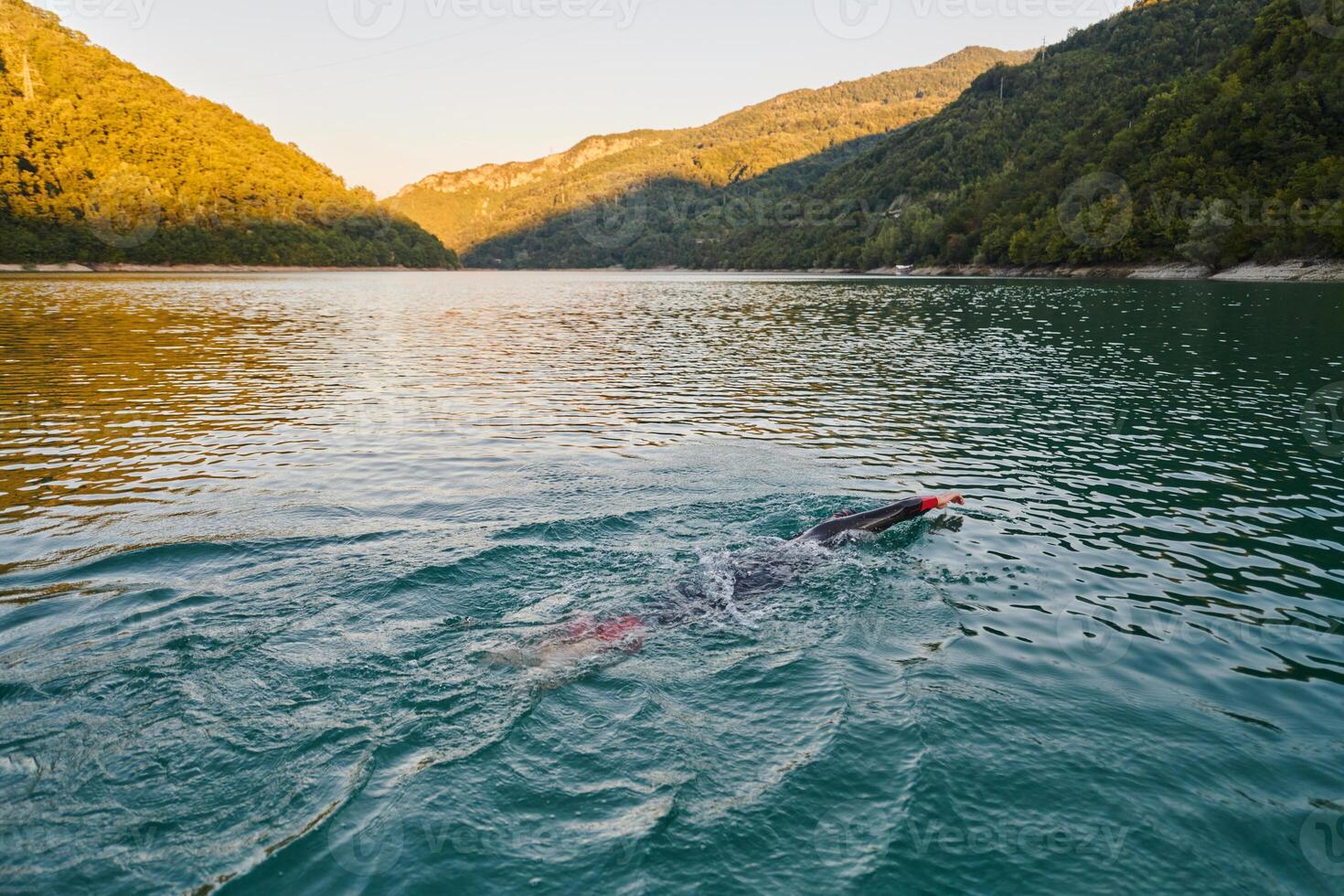 Triathlon athlete swimming on lake in sunrise wearing wetsuit photo