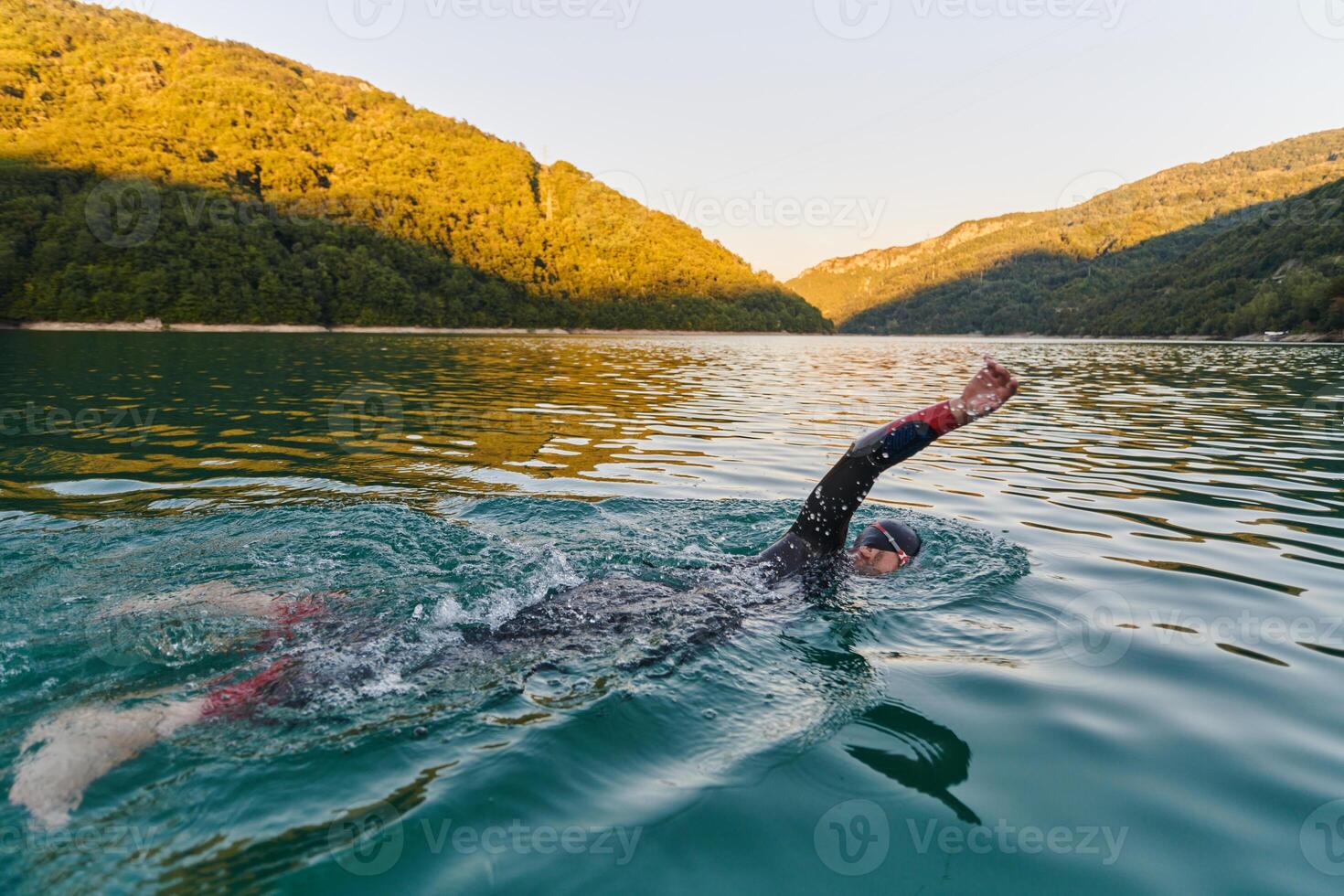 Triathlon athlete swimming on lake in sunrise wearing wetsuit photo