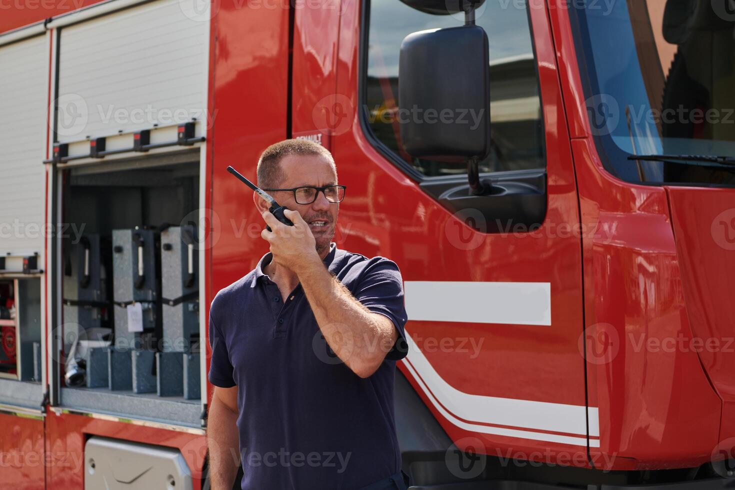 A dedicated firefighter, captured in a moment of communication, stands before a modern firetruck, showcasing the seamless integration of technology in emergency response photo