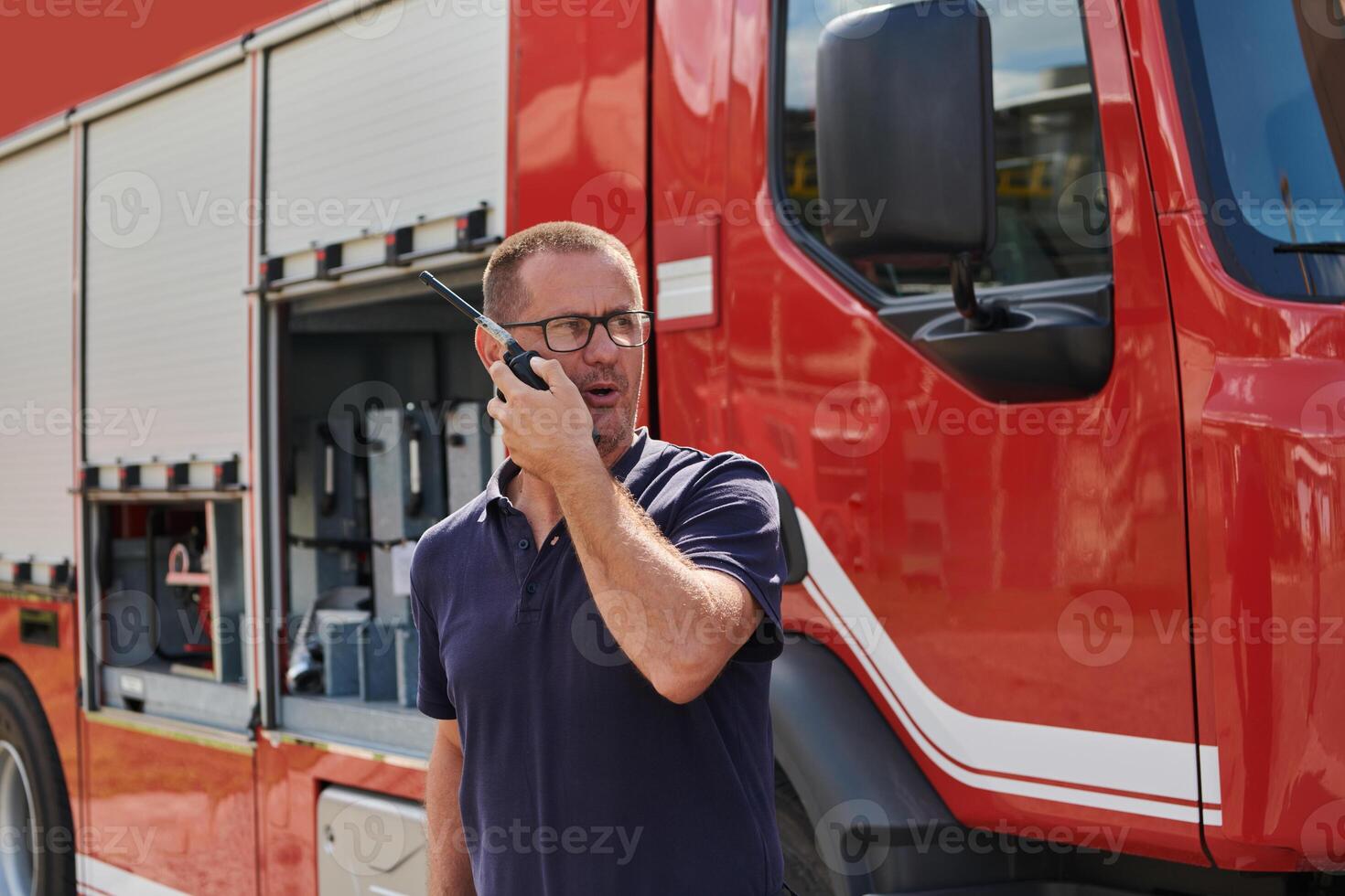 A dedicated firefighter, captured in a moment of communication, stands before a modern firetruck, showcasing the seamless integration of technology in emergency response photo