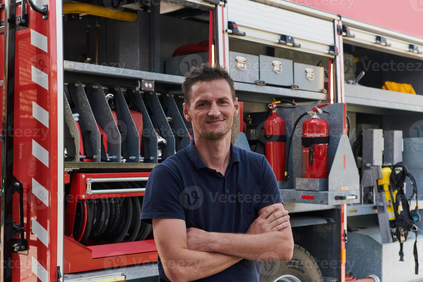 Confident firefighter stands with crossed arms, exuding resilience and preparedness, ready to respond to emergencies alongside a modern fire truck, showcasing the heroism and strength of the fire photo