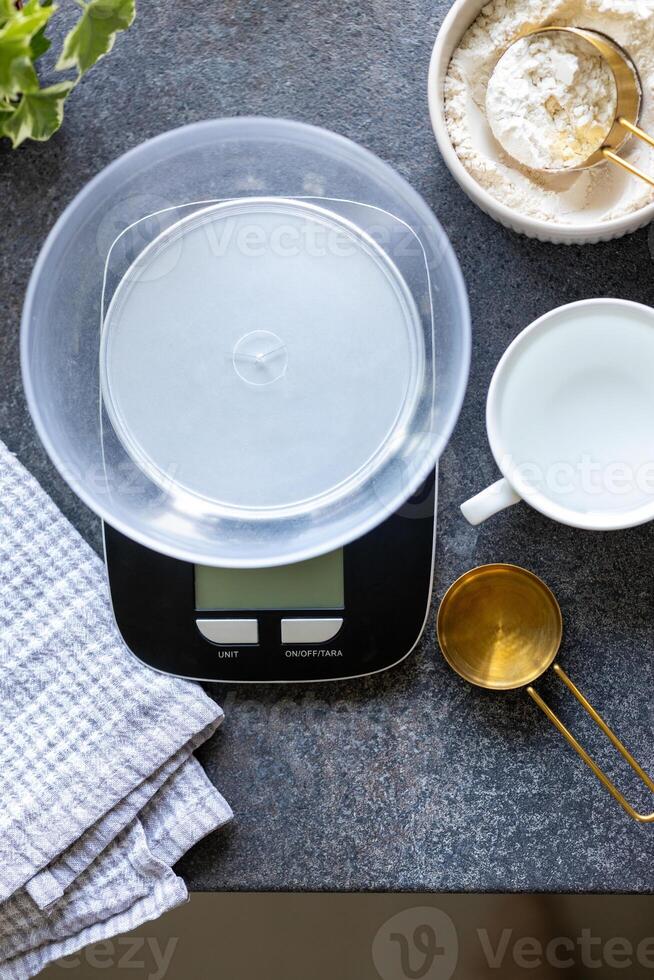 Scales, measuring spoon, napkin, water and flour on concrete kitchen counter photo