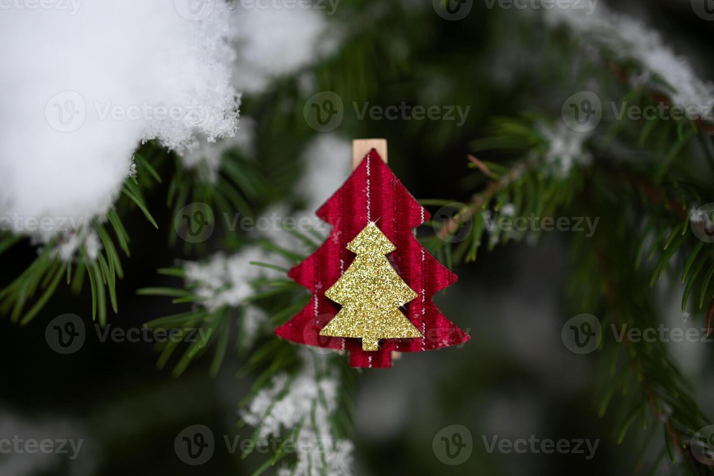Red Christmas ornament in shape of fir tree on snow-covered Christmas tree branch outdoors. Selective focus, close-up photo