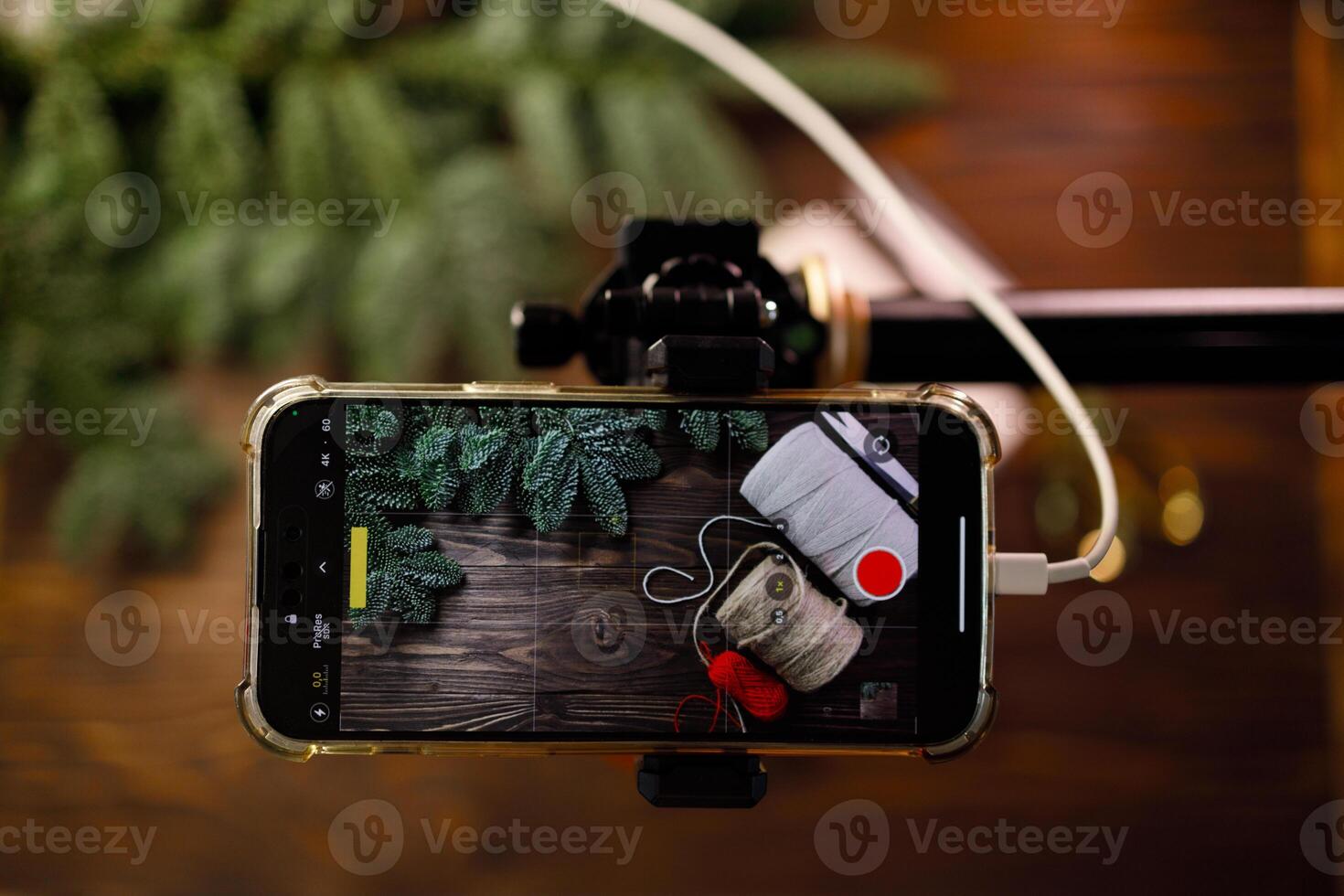 POV phone shooting photo or for vlog with craft supplies on wooden table decorated with spruce branches. Concept of filming tutorial for web vlog about handmade crafting. Xmas and winter leisure