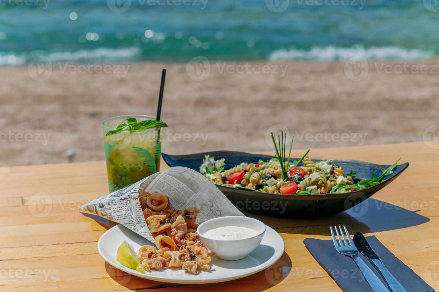 Crispy fried squid with aioli and salad with pasta on table photo