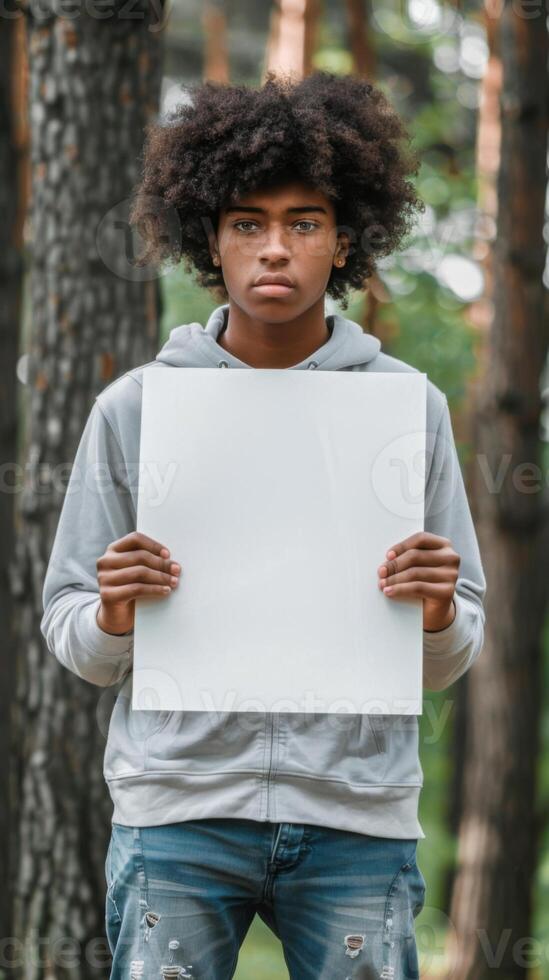 A young man with a black afro holds a blank sign in the woods photo