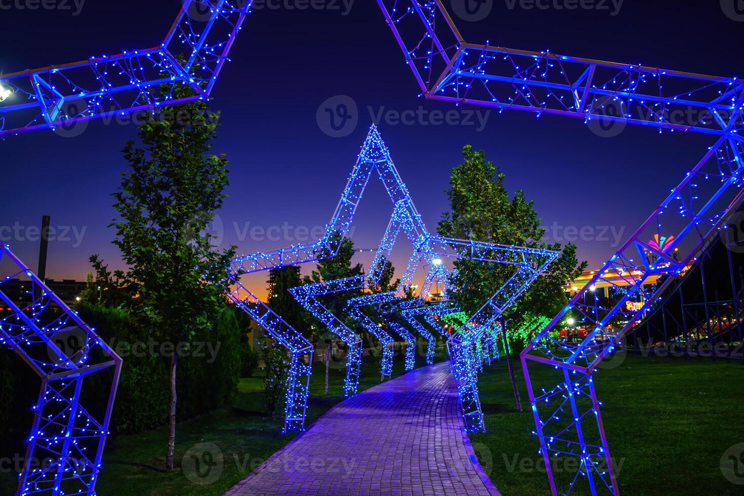 Decorations in the form of arches in the form of stars from LED lighting over the pavement in the night amusement park. photo