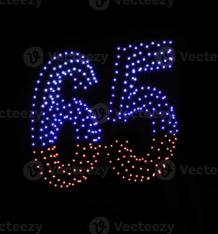 Drone light shows on black night sky background. A figure of the number six, five, sixty five, 65 made of glowing drones. photo
