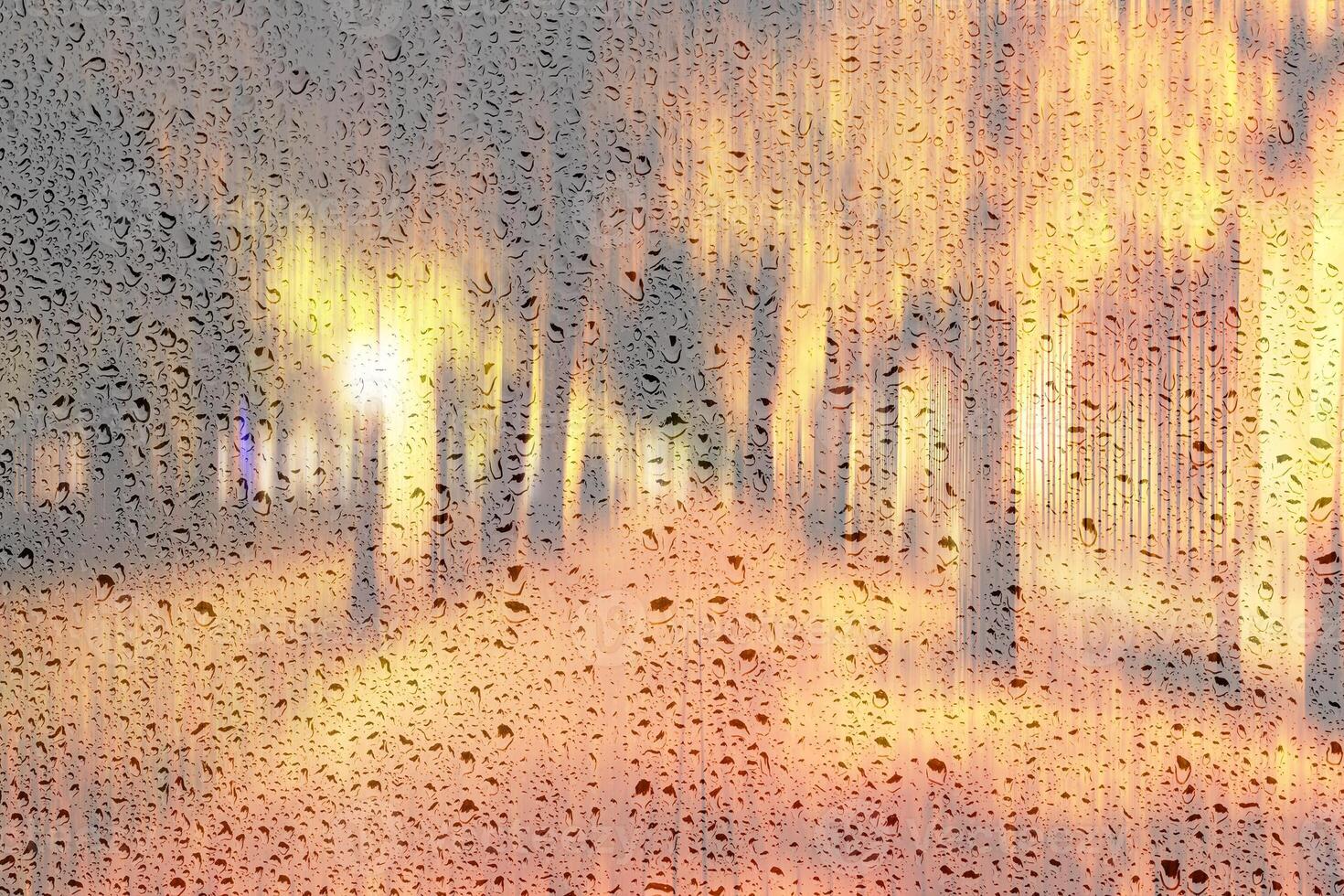 Night rainy park with yellow maple leaves, pavement and lanterns behind wet rainy glass in golden autumn. The concept of bad weather, change of season and leaf fall. Abstract landscape. photo