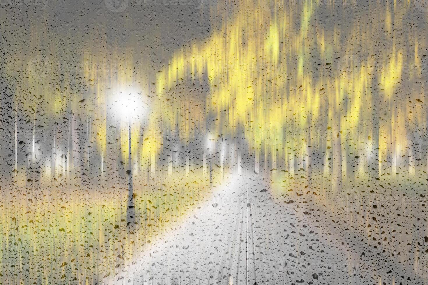 Night rainy park with yellow maple leaves, pavement and lanterns behind wet rainy glass in golden autumn. The concept of bad weather, change of season and leaf fall. Abstract landscape. photo