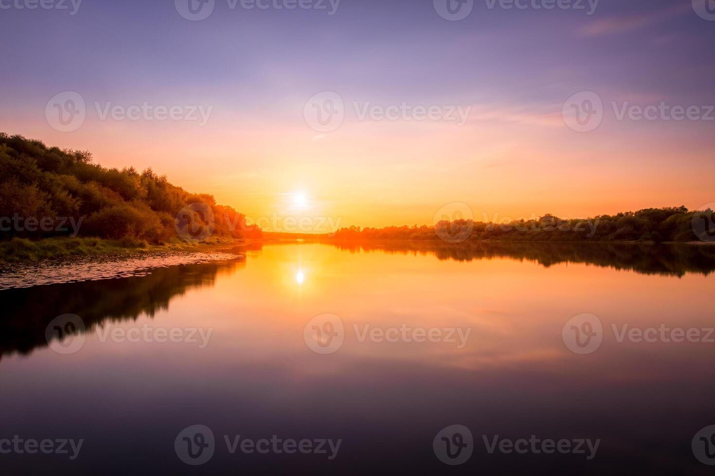 Sunset or dawn on a river with a cloudy sky and sun rays reflected in the water, water lilies and trees growing along the shore. photo