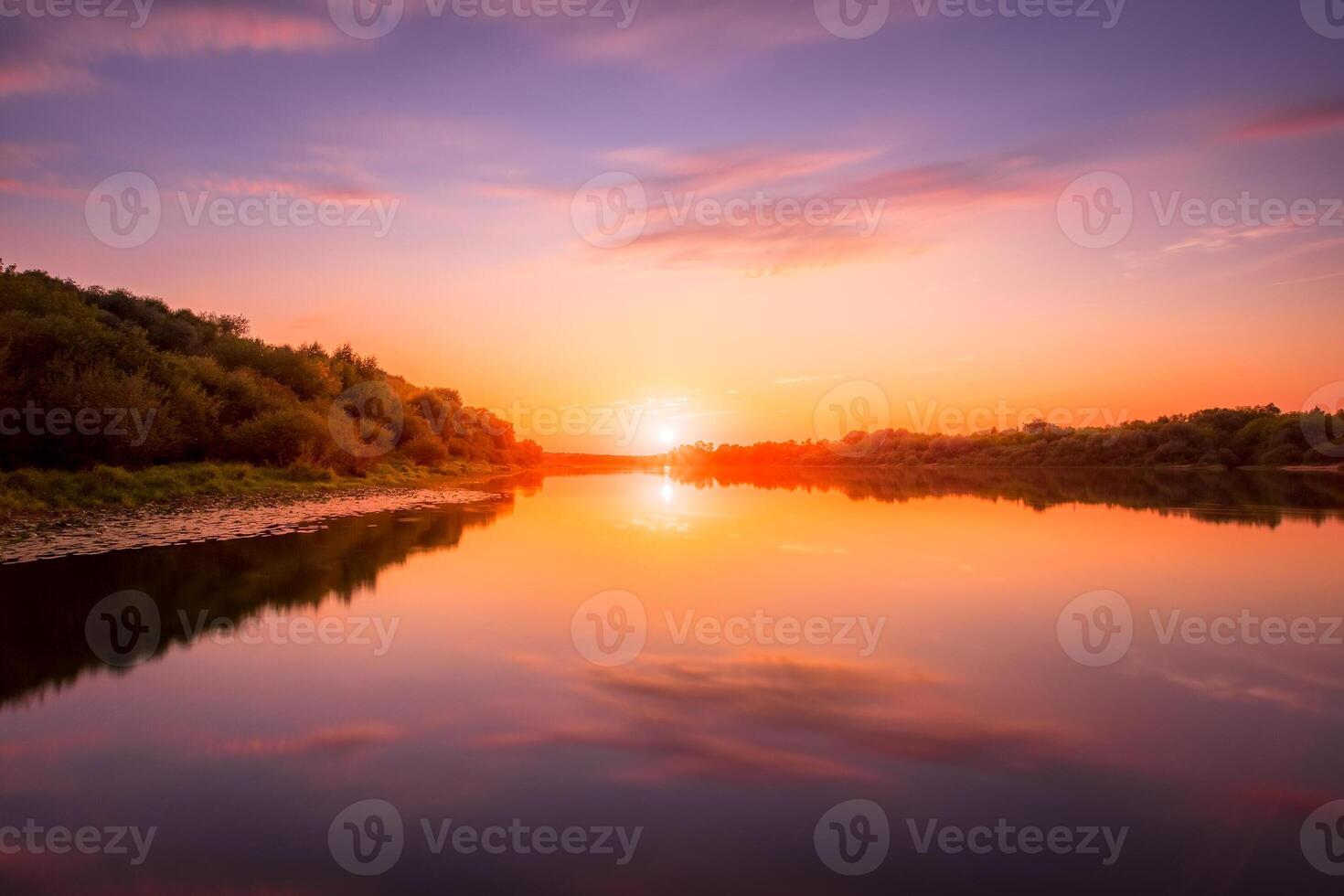 Sunset or dawn on a river with a cloudy sky and sun rays reflected in the water, water lilies and trees growing along the shore. photo