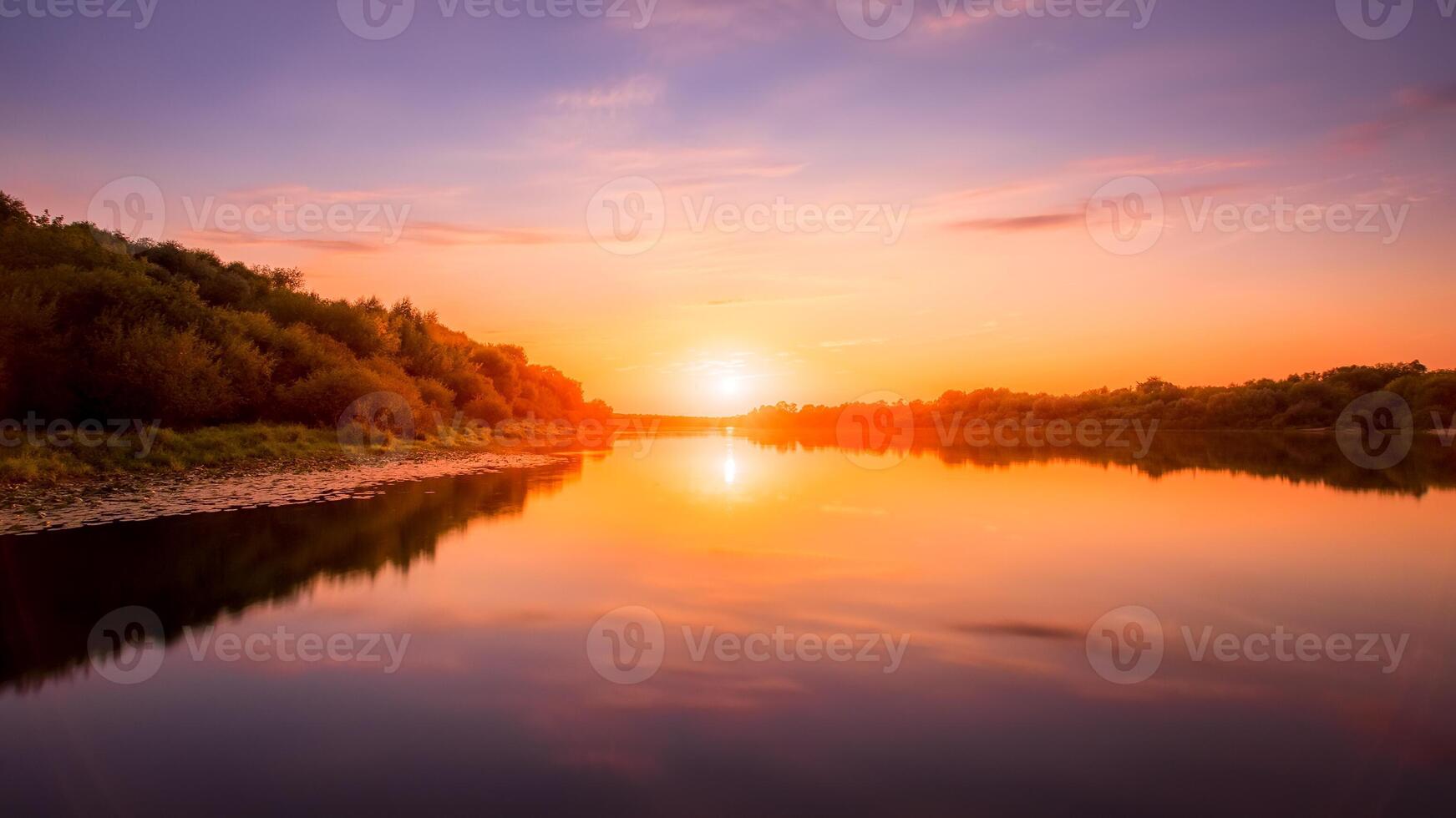 Sunset or dawn on a river with a cloudy sky and sun rays reflected in the water, water lilies and trees growing along the shore. photo