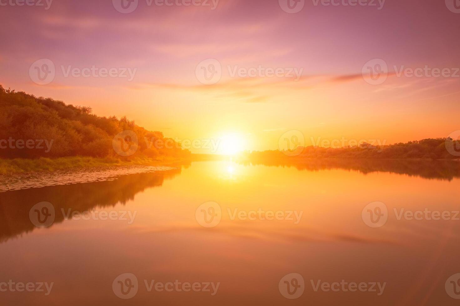 Sunset or dawn on a river with a cloudy sky and sun rays reflected in the water, water lilies and trees growing along the shore. photo